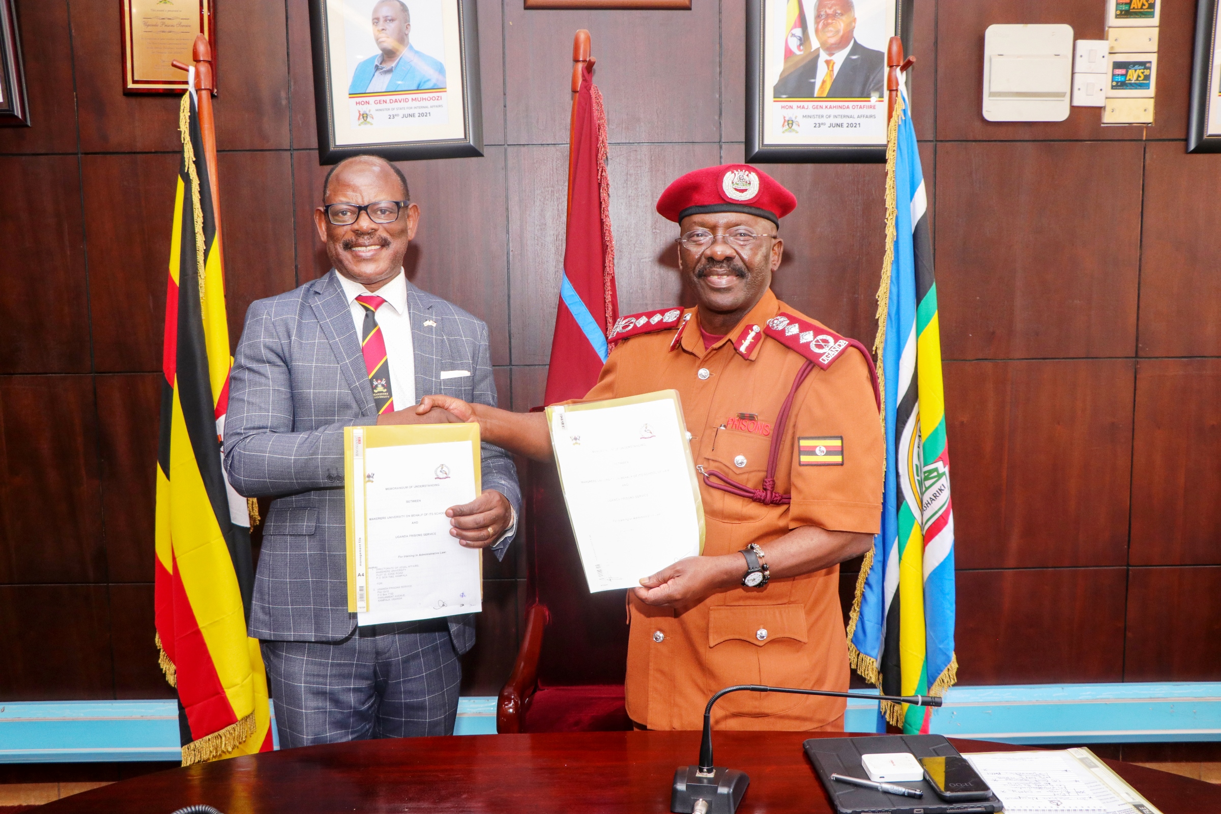 Prof. Barnabas Nawangwe (Left) and Dr. Johnson Byamugisha (Right) shake hands as they display the signed Memorandum of Understanding. Makerere University and Uganda Prison Services (UPS) sign Memorandum of Understanding that paves way for Makerere University School of Law to undertake short trainings in administrative law for UPS staff, 10th December 2024, Kampala Uganda, East Africa.