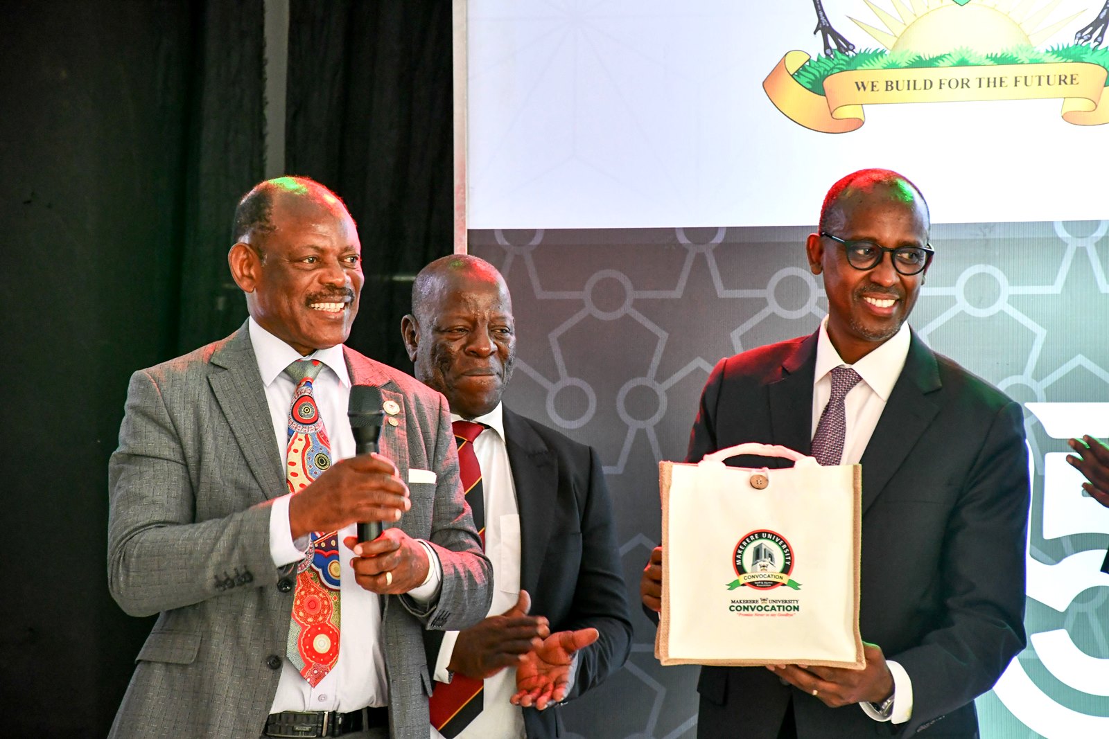 Mr. Odrek Rwabwogo (Right) shows off his gift from the Convocation as Prof. Barnabas Nawangwe (Left) and Engineer Isaac Mubarak Ngobya (Centre) applaud. 75th Graduation Ceremony, Day 3, MUBSS. Convocation Luncheon, 15th January 2025, Edge Road, Makerere University, Kampala Uganda, East Africa.