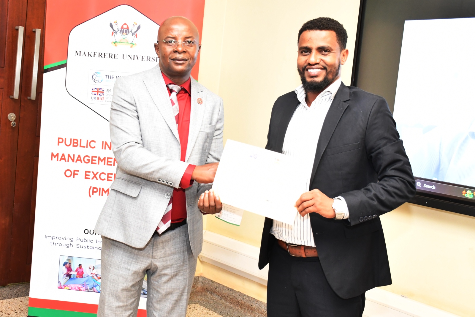 Principal CoBAMS-Prof. Edward Bbaale (Right) presents a certificate to one of the officials. Six Somali government officials three-day Executive Training in Infrastructure Asset Management, held at Public Investment Management Centre of Excellence (PIM CoE), College of Business and Management Sciences (CoBAMS), funded by the United Nations Capital Development Fund (UNCDF), 27th-29th January 2025, aimed to enhance regional capacity in infrastructure planning and management, Yusuf Lule Central Teaching, Makerere University, Kampala Uganda, East Africa.