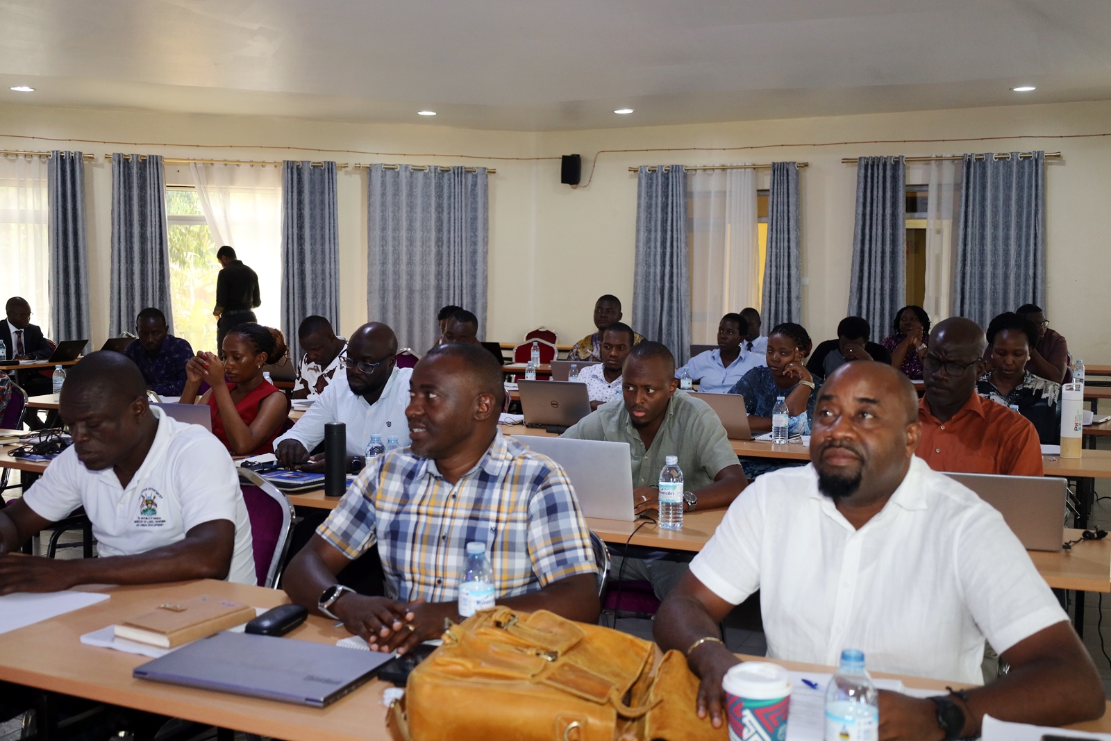 A section of participants follows proceedings. Public Investment Management (PIM) Centre of Excellence, College of Business and Management Sciences (CoBAMS), Makerere University, Kampala, Day 1 of three-day refresher training for members of the Development Committee (DC) of the Ministry of Finance, Planning and Economic Development, 19th February 2024, Jinja Uganda, East Africa.