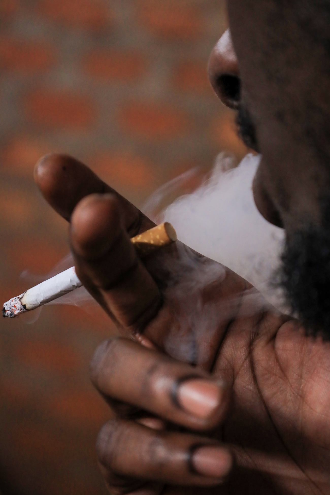 A young man smokes cigarettes in Makerere Kikoni, a neighborhood bordered by Bwaise to the north, Makerere University to the east, Naakulabye to the southwest. Formerly a slum in semi permanent structures, it is now most developed with student hostels. Makerere University School of Public Health (MakSPH), Kampala Uganda, East Africa.