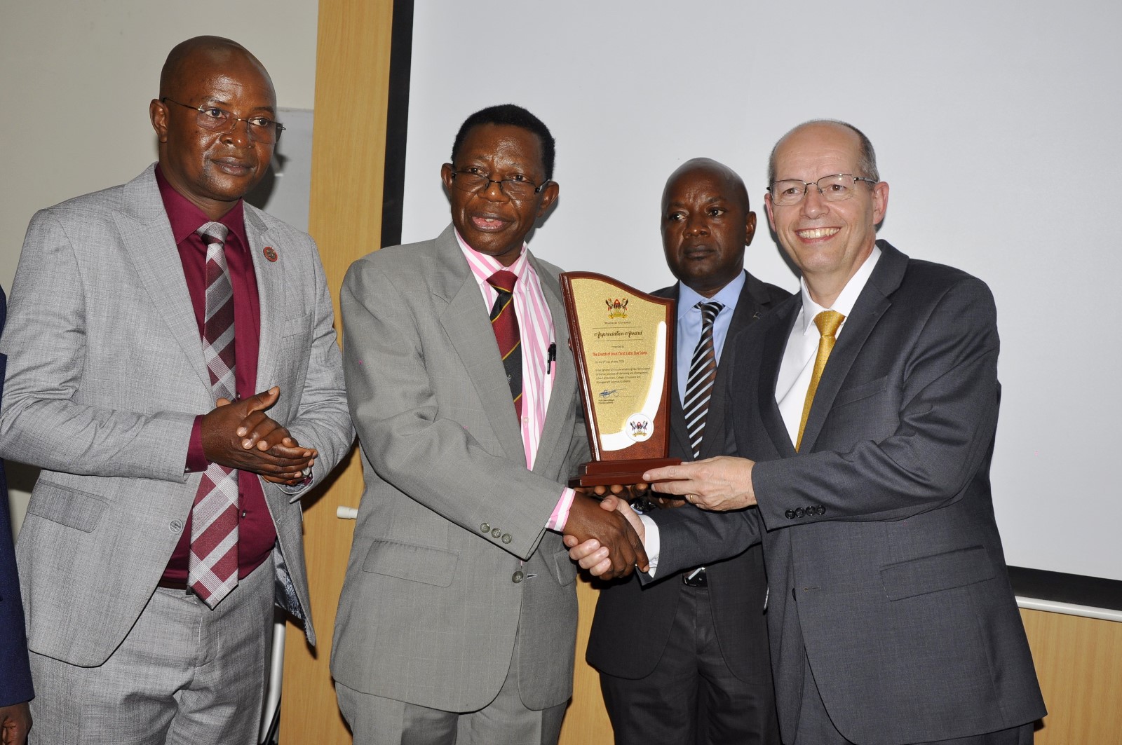 Professor Buyinza presents a plaque to Brother Christophe as Professor Bbaale and Dr. Tibaingana witness. Church of Jesus Christ of Latter-day Saints handed over 40 high-tech laptops and 10 projectors to Makerere University to facilitate teaching, learning, and research at the School of Business under the College of Business and Management Sciences (CoBAMS), 5th May 2025, Kampala Uganda, East Africa.
