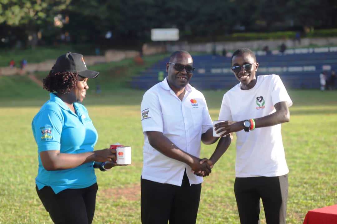 Mr. John Osuna (Centre) presents a gift to a participant. Mastercard Foundation Scholars Program family day event, 19th May 2025, Rugby Grounds, Makerere University, Kampala Uganda, East Africa.