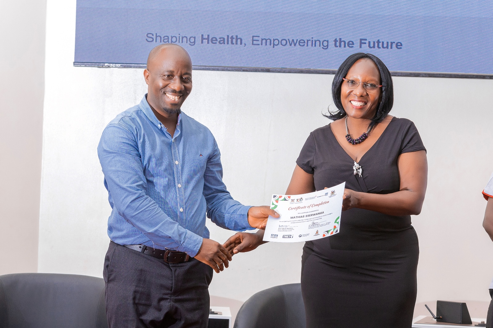 Dr. Sarah Byakika awarding a certificate to the Cohort President, Mr. Mathias Sserwanga, the In-charge of Namulonge Health Centre III in Nansana Municipality during the workshop on April 23, 2025. Makerere University School of Public Health (MakSPH) disseminating outcomes of a major leadership and management strengthening initiative in Wakiso District, Central Uganda. The one-year project, part of the Global Health Partnerships programme funded by NHS England implemented in collaboration with Nottingham Trent University, Nottingham University Hospitals NHS Trust, Wakiso District Local Government, and Uganda’s Ministry of Health, 23rd April 2025, MakSPH Auditorium, Kampala, East Africa.