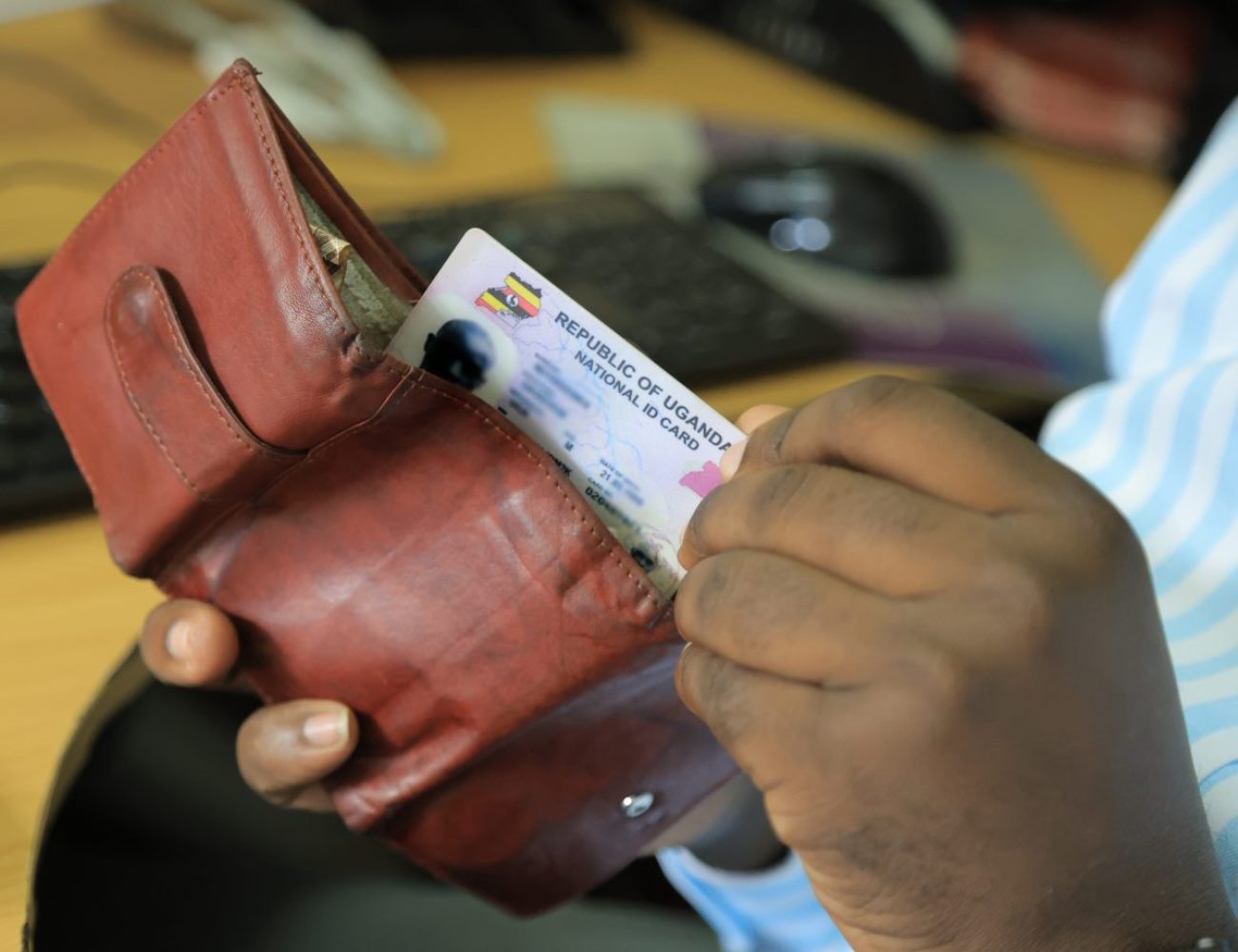 A man reaches for the Uganda National ID from his wallet. New study, “Understanding the Benefits, Costs, and Challenges of the National Identification System in Uganda,” published in Digital Society, for every US$1 invested in the NID system, the return on investment is US$1.35, led by Roy William Mayega from Makerere University School of Public Health’s Resilient Africa Network (MakSPH-RAN), Kampala, Uganda, East Africa.