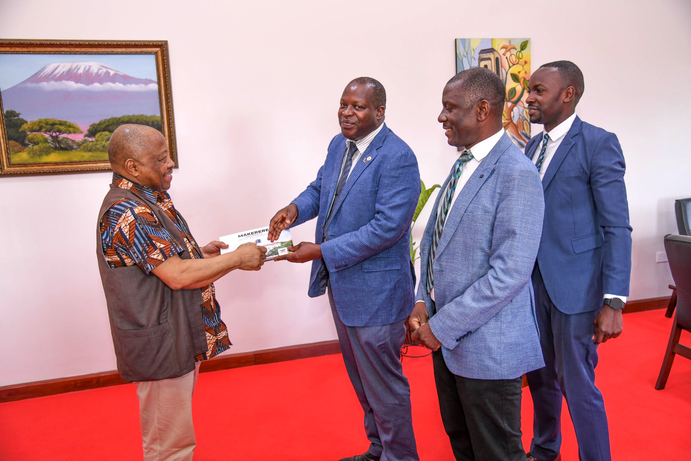 Prof. Omotade Akin Aina (Left) receives the Makerere Souvenir Book from Prof. Tonny Oyana as Prof. Julius Kikooma (2nd Right) and Mr. Charles Lwanga (Right) witness. Prof. Omotade Akin Aina-Carnegie Corporation of New York meeting to discuss progress of Consolidating Early Career Academics Programme (CECAP) phase II, which focuses on fostering academic development and research among early-career academics, 23rd May 2025, Main Building, Makerere University, Kampala Uganda, East Africa.