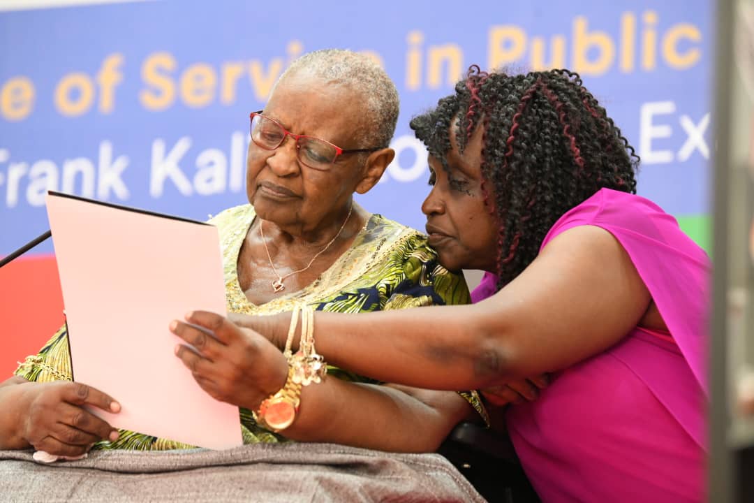 Mrs. Esther Kalimuzo assisted by her daughter delivers her remarks. 2nd Frank Kalimuzo Memorial Lecture, theme ‘Building a culture of service in Public Institutions’ organised in partnership with Makerere University Business School (MUBS), 13th June 2025, Main Hall, Makerere University, Kampala Uganda, East Africa.