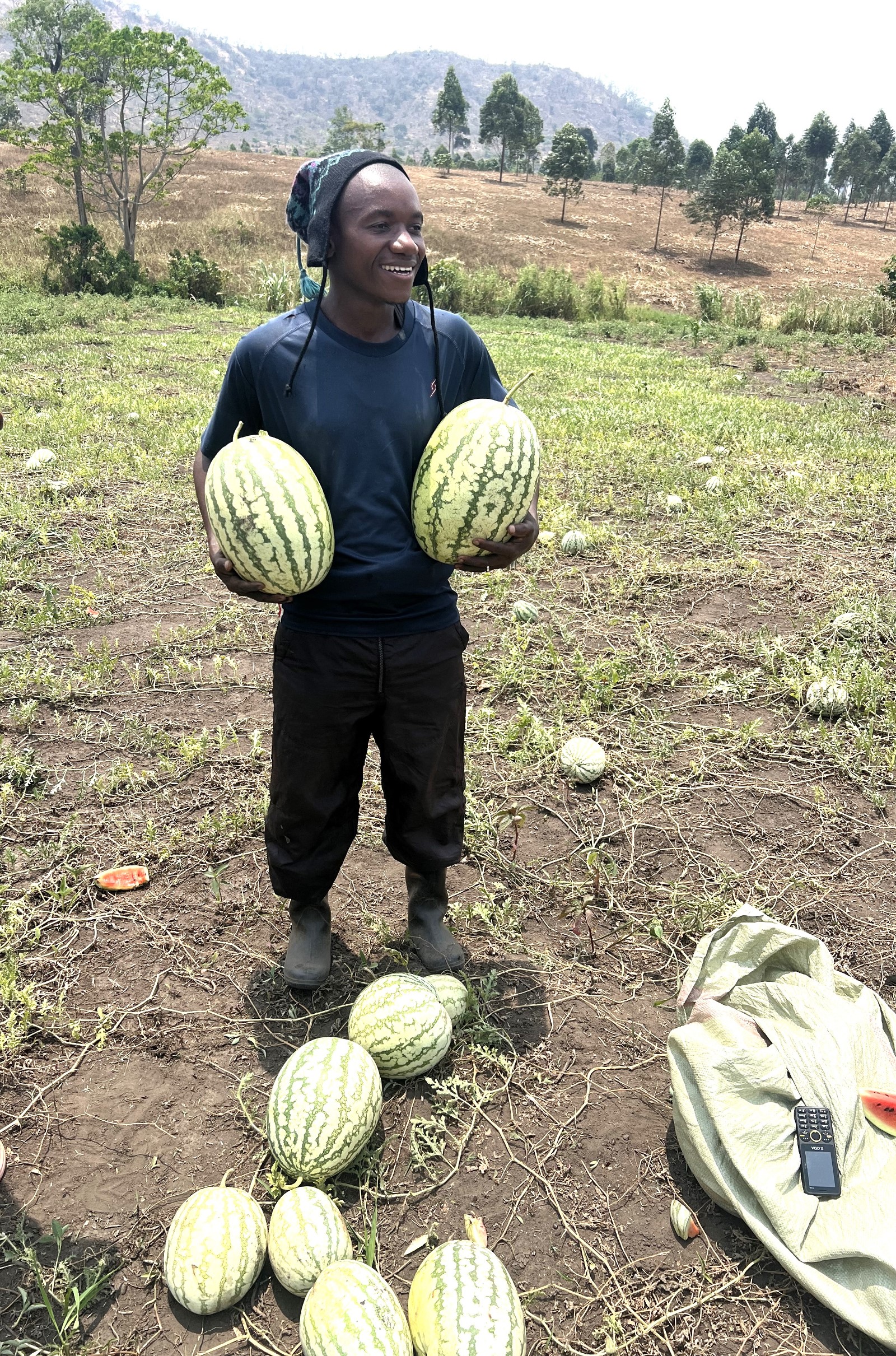 One of the refugee young men excited with his harvest of watermelon, a result of the training offered by Safali Libia in Kyangwali Refugee Settlement. Mastercard Foundation Scholars Program at Makerere University, International World Refugee Day 2025, themed “solidarity with refugees,” highlights of remarkable achievements of Scholars and alumni with refugee backgrounds, June 2025, Kampala Uganda, East Africa.
