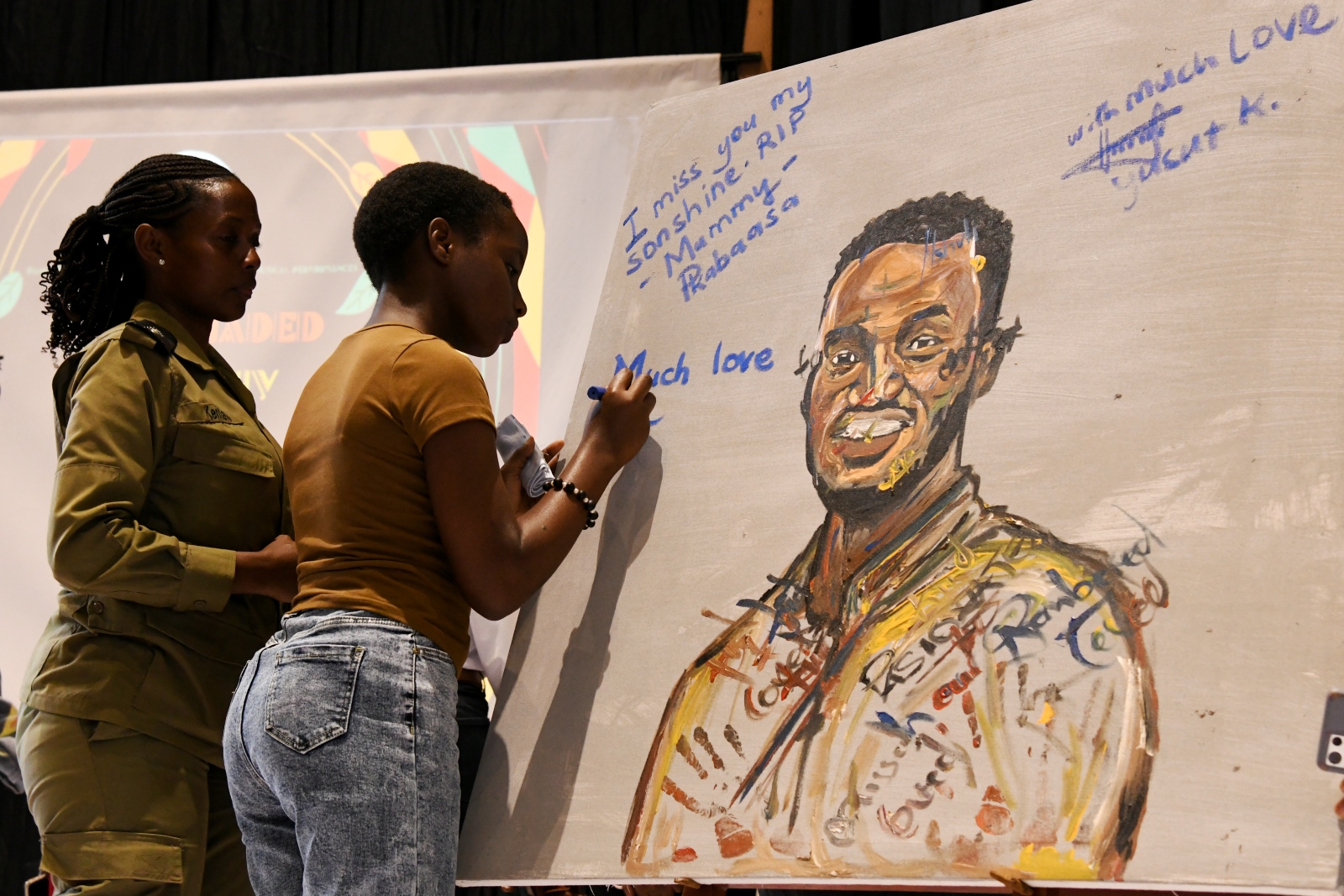 Mrs. Pamela Mbabazi witnesses as her daughter autographs the memorial art piece. 3rd edition of Hadithi Ya Mzizi to celebrate the resilience and innovation of the informal sector through art exhibition and to memorialize its founder, the late Nshuti Balaam Kabaasa, 29th August 2025 Makerere University, Kampala Uganda, East Africa.