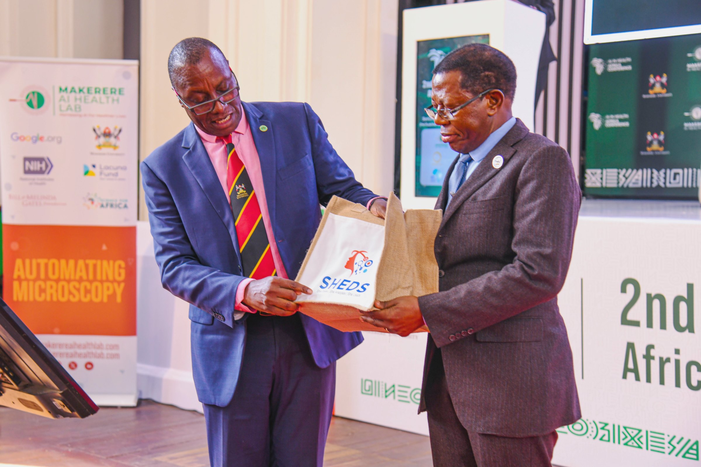 Prof. Buyinza Mukadasi (Right) receives a SHEDS gift pack from Dr. Andrew Kambugu (Left). 2nd Artificial Intelligence (AI) in Health Africa Conference under theme “Setting AI for Sustainable and Inclusive Health Systems in Africa”, Opening Ceremony 6th November 2025, Main Hall, Makerere University, Kampala Uganda, East Africa.