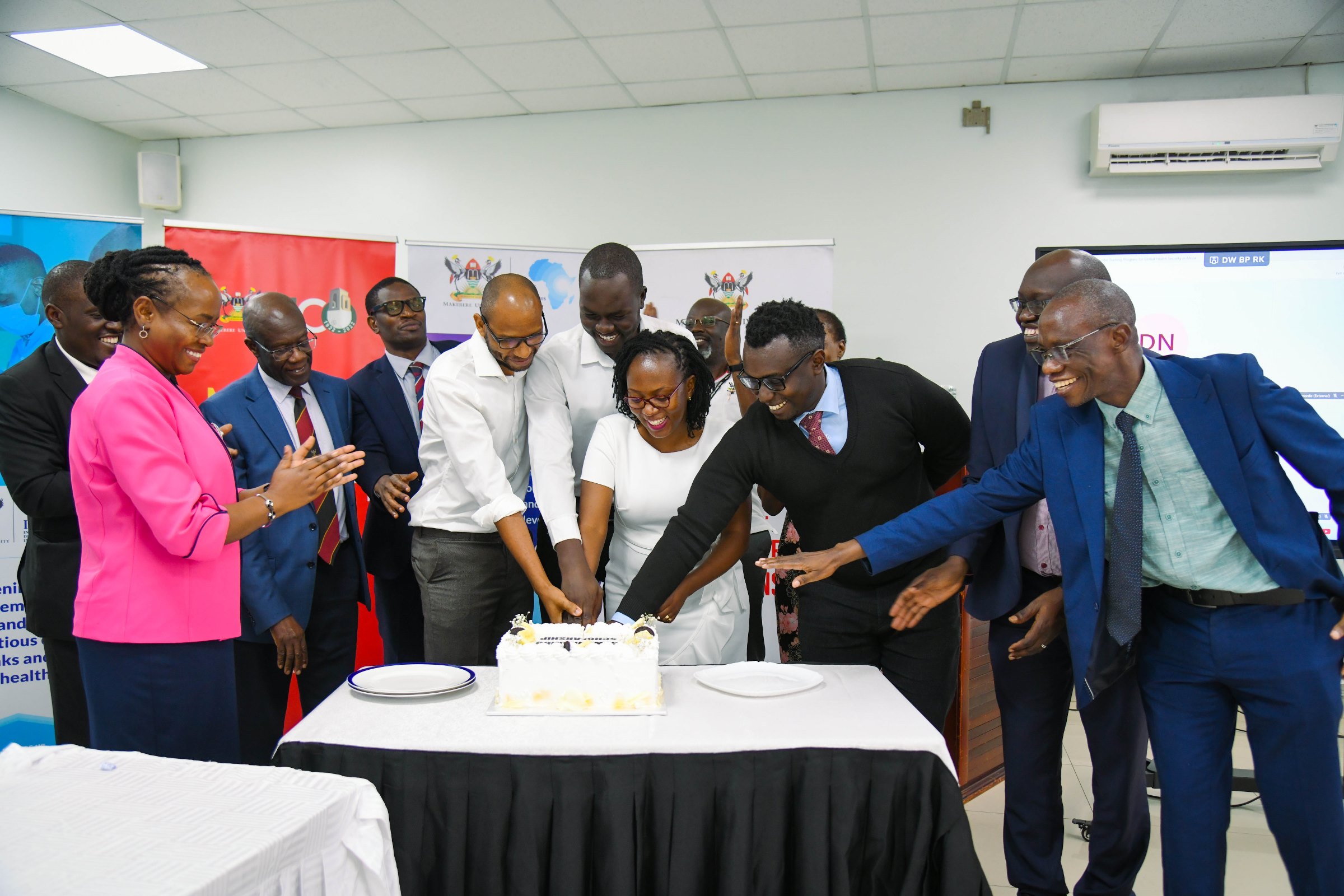 Cohort 2 PhD fellows cut cake as officials applaud. Makerere University Infectious Diseases Institute (IDI) unveils second cohort of PhD Fellows and launch of Sewankambo Training Program for Global Health Security, 27th November 2025, Makerere University, Kampala Uganda, East Africa.