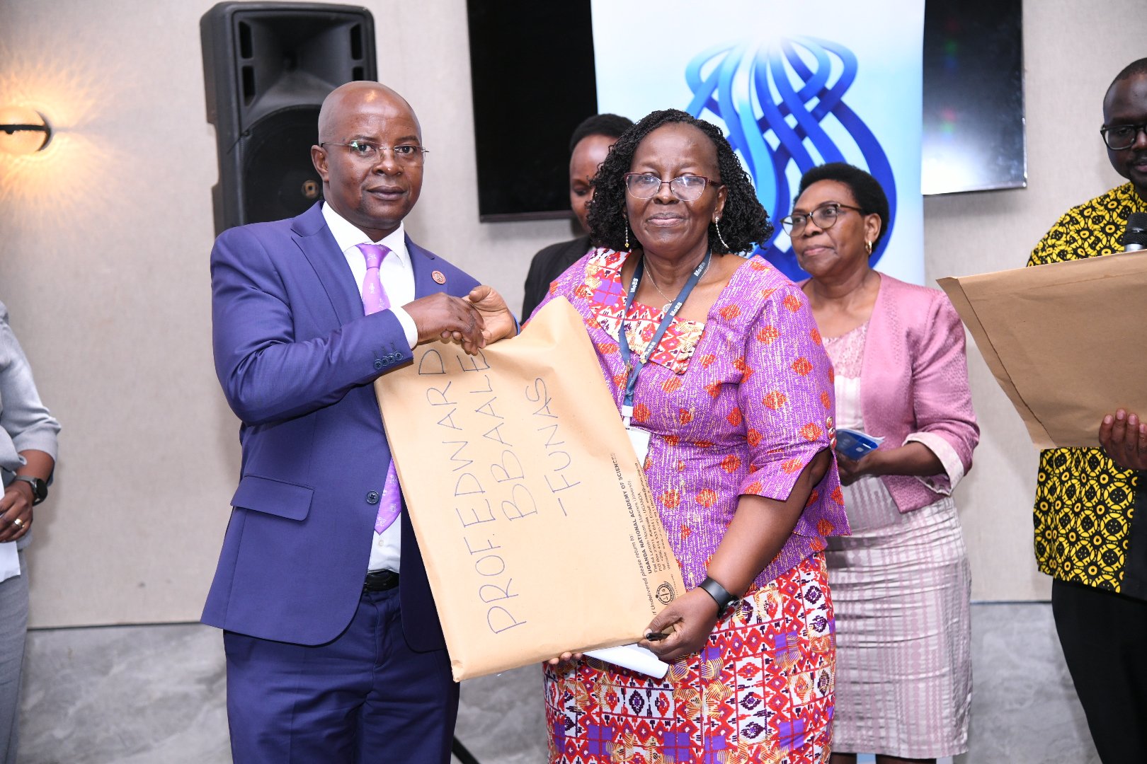 The President UNAS Council-Prof. Grace Bantebya Kyomuhendo (Right) presents induction documentation to Prof. Edward Bbaale (Left) as Council Members (Background) witness on 31st October 2025. Professor Edward Bbaale, Principal of the College of Business and Management Sciences (CoBAMS), Makerere University, inducted into the prestigious fellowship of the Uganda National Academy of Sciences (UNAS), 31st October 2025, Kampala Uganda, East Africa.
