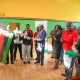 Prof. Barnabas Nawangwe hands the Makerere flag over to Team Captain-Namutebi Rhonah Majoline as Dr. Winifred Kabumbuli (3rd Right), Mr. Brian Miiro (2nd Right) and Left to Right: Dr. Rodney Rugyema, Phillip Nuwagaba, Katsirabo Donic, Akampa Bob James and others applaud on 17th December 2025 in the Mak Indoor Sports Arena. Prof. Barnabas Nawangwe officially flags off a contingent of 220 students, 13 coaches and 3 tutors from the Makerere University Games Union on 17th December 2025 at the Indoor Sports Arena to the 20th Edition of the Association of Uganda University Sports (AUUS) Games, 18th-23rd December 2025, Uganda Christian University (UCU) Mukono, Uganda, East Africa.