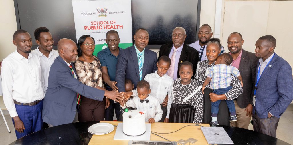 Faculty members join Dr. Ntaro, his family, and friends in a celebratory cake-cutting shortly after the defence. Makerere University School of Public Health Communications Office, Graduation Profiles Series, 76th Graduation Ceremony, Moses Ntaro, “Effect of Student Community Engagement on Open Defecation-Free Status,” Kampala Uganda, East Africa.