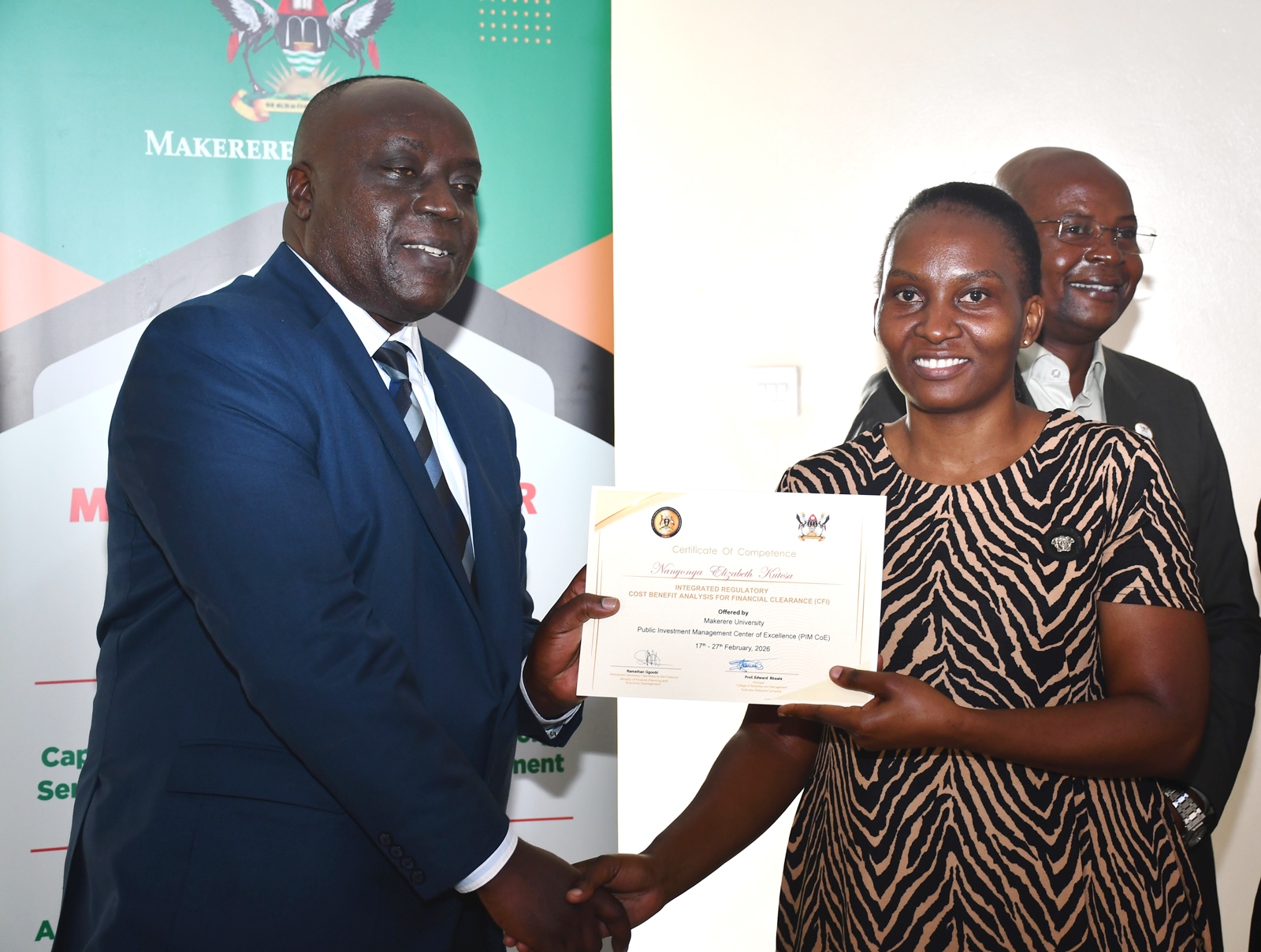 Commissioner Mwanja presents a certificate to one of the participants Nanyonga Elizabeth Kutesa. In the background is Prof. Edward Bbaale. Ministry of Finance, Planning and Economic Development (MoFPED), in partnership with the Public Investment Management Centre of Excellence (PIM CoE), Makerere University, Kampala in collaboration with the Infrastructure and Social Services Department (ISSD) and the National Planning Authority (NPA), successful completion of two-week intensive training in the Certificate of Financial Implications (CFI) – Integrated Regulatory Cost-Benefit Analysis (IRCBA). 27th February 2026, Pearl on the Nile Hotel, Jinja, Uganda, East Africa.