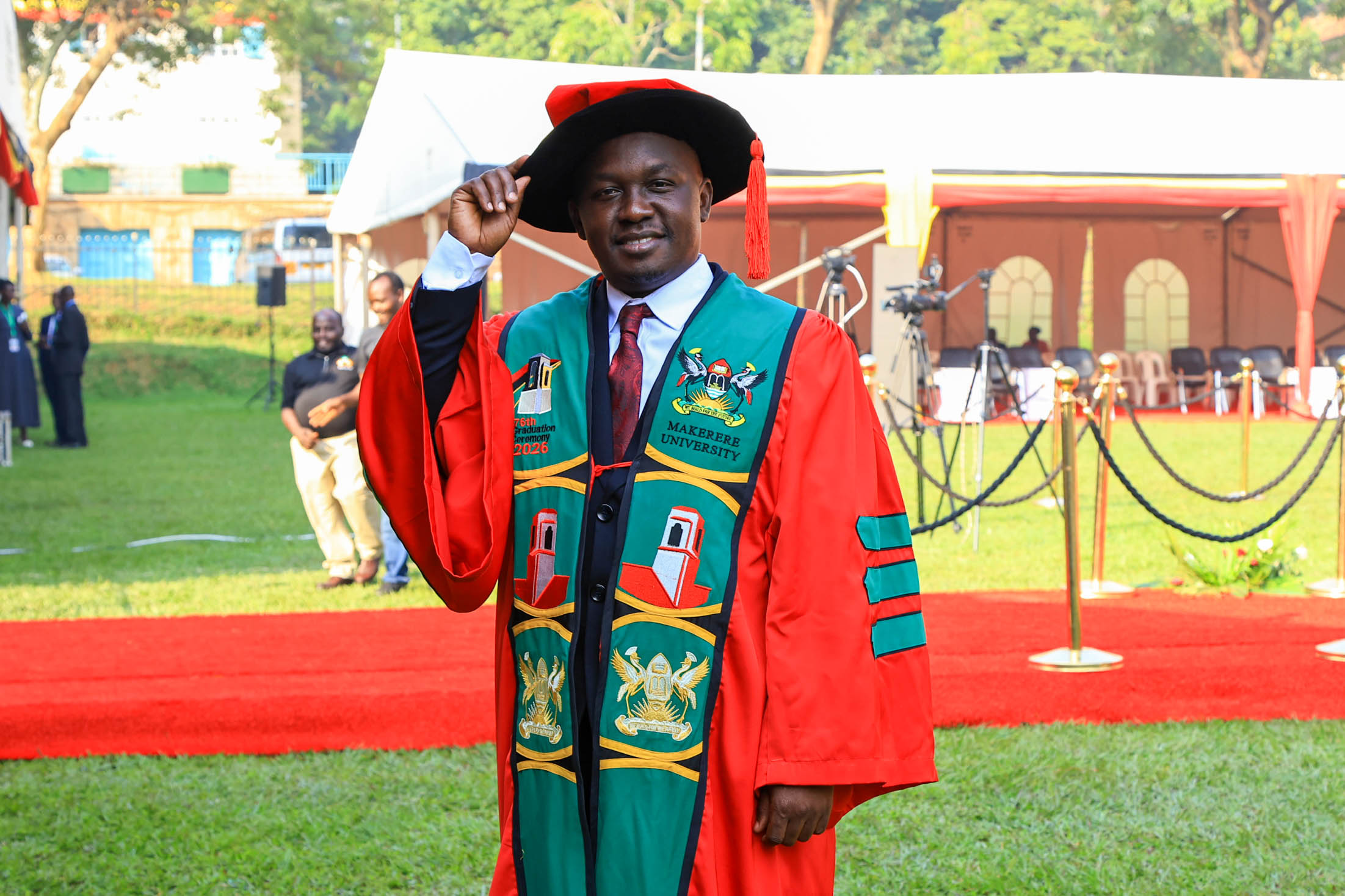 Henry Komakech adjusts his doctoral bonnet after being conferred the Doctor of Philosophy (Public Health) degree during Makerere University’s 76th Graduation Ceremony at Freedom Square on February 25, 2026. Makerere University School of Public Health Communications Office, Graduation Profiles Series, 76th Graduation Ceremony, Dr. Henry Komakech, “Effects of the Repatriation of Refugees on the Health Services of the Host Populations in the West Nile Districts of Arua, Moyo, and Adjumani,” Kampala Uganda, East Africa.