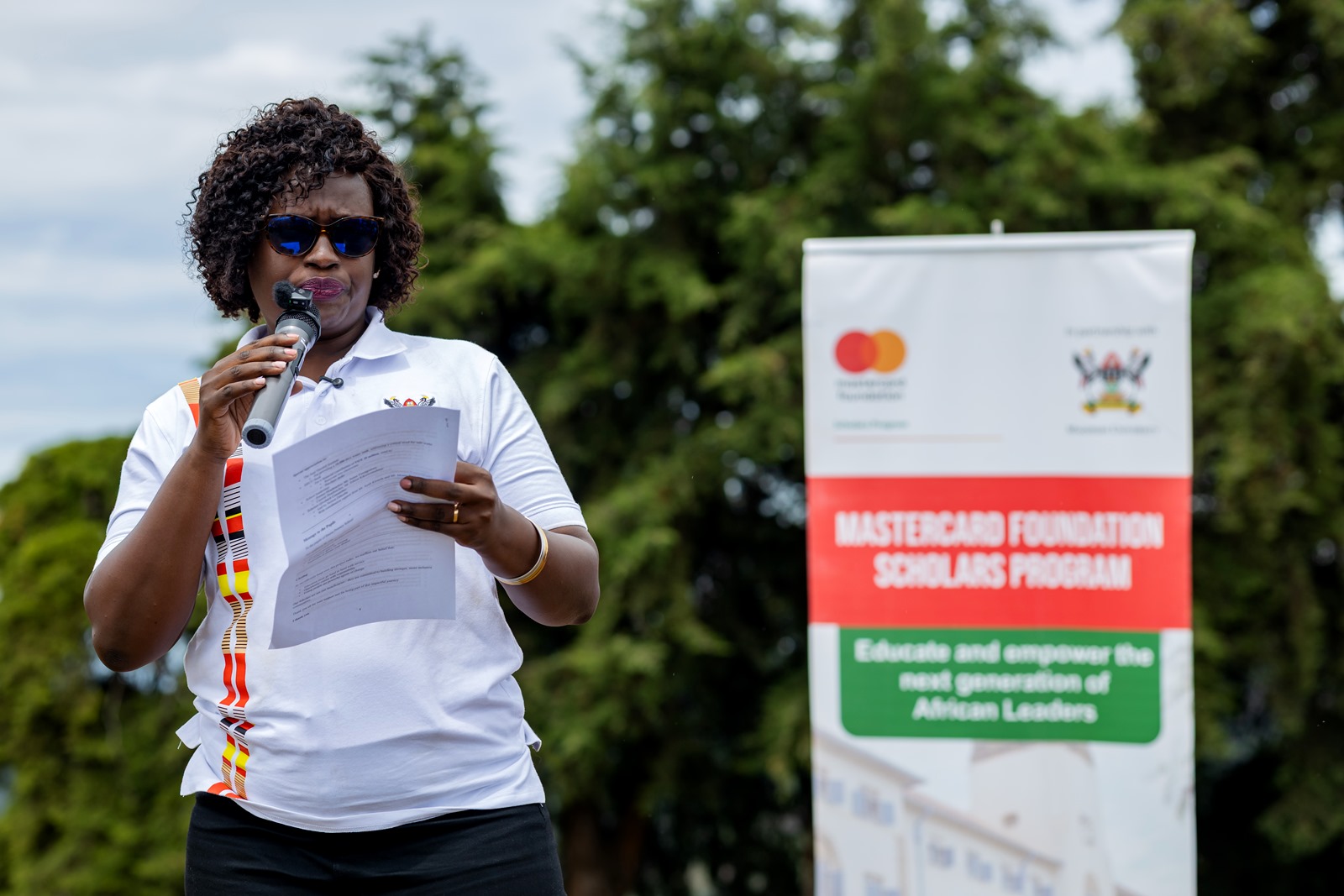 Ms. Jolly Okumu speaks at the Mastercard Foundation Scholars Program at Makerere University Giveback to Bwera Primary School, Kabale in partnership with dfcu Bank on 1st April 2026. Mastercard Foundation Scholars Program at Makerere University Giveback, in partnership with dfcu Bank, handover five-classroom block equipped with 60 bench desks, four-stance modern pit latrine, and a 10,000-litre rainwater harvesting system on 1st April 2026 to Bwera Primary School in Kabale District, Uganda, East Africa.