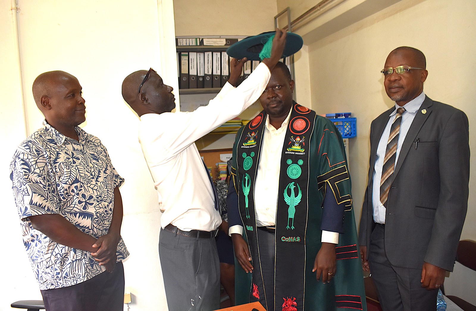 Mr. Patrick Akonyet completes the robing of Prof. Ssevviiri in the Dean’s academic regalia with the cap. Prof. Michael Owor officially hands over office of Dean, School of Physical Sciences to Prof. David Ssevviiri for the next four years, effective 6th May 2026, on 28th May 2026, College of Natural Sciences (CoNAS), Makerere University, Kampala Uganda, East Africa.