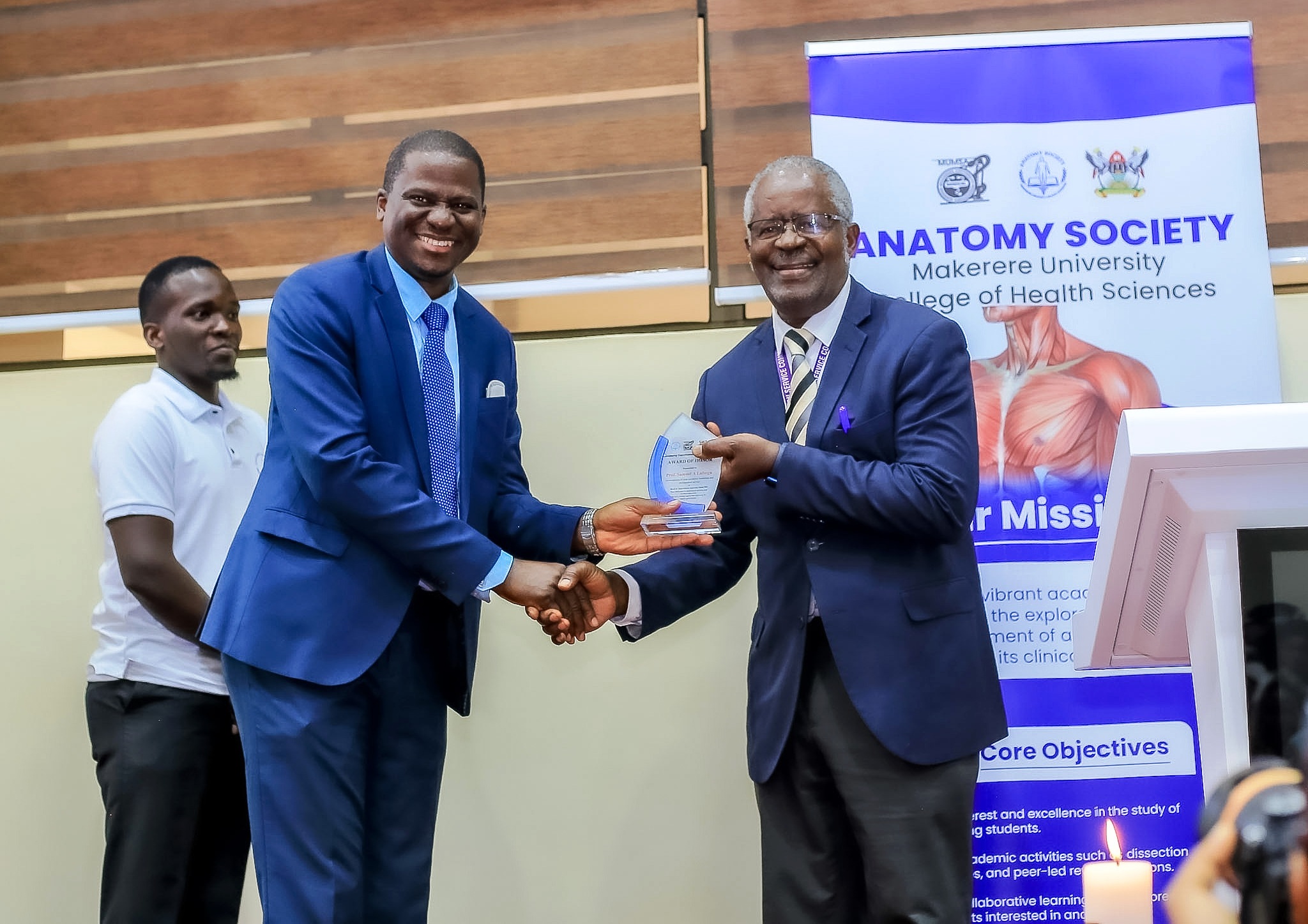 Prof. Elisa Mwaka (L) presents a plaque to keynote speaker, Rev. Prof. Dr. Samuel Luboga at the Second Cadaver Commemoration Ceremony on 11th June 2026. Second Cadaver Commemoration Ceremony organized by the Makerere Students' Anatomy Society under the Department of Anatomy, College of Health Sciences (CHS) on June 11, 2026 at Makerere University School of Public Health Auditorium, Main Campus, Eastern Gate, Kampala Uganda, East Africa.