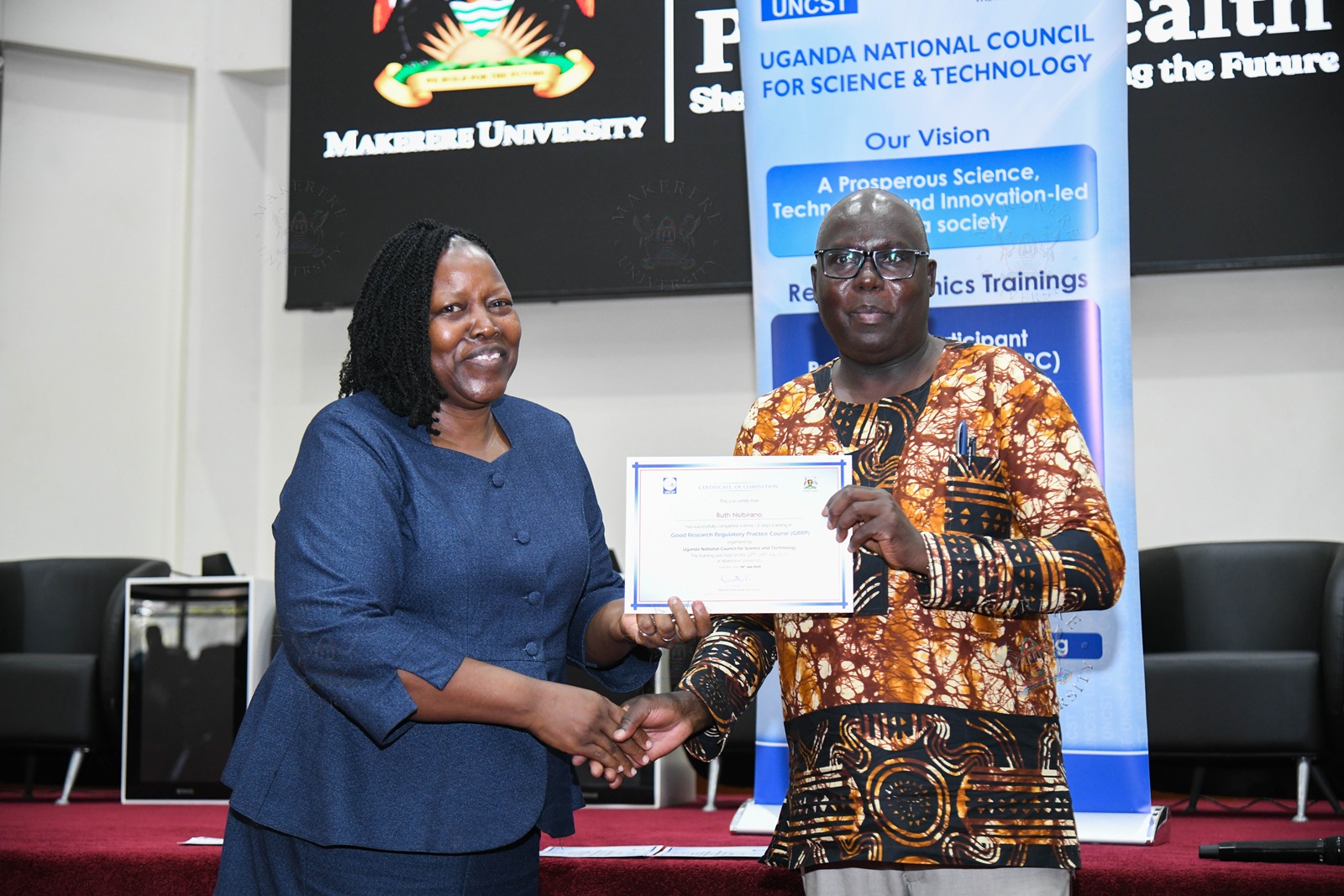 Dr. Martin Patrick Ongol (R) presents a certificate to Prof. Ruth Nsibirano (L). Closing Ceremony of the three-day Good Research Regulatory Practice (GRRP) Course for members of Research Ethics Committees (RECs) from Makerere University and other institutions organized by the Directorate of Research, Innovations and Partnerships (DRIP) at Makerere University in partnership with the Uganda National Council for Science and Technology (UNCST), 24th July 2026, MakSPH Auditorium, Kampala Uganda, East Africa.