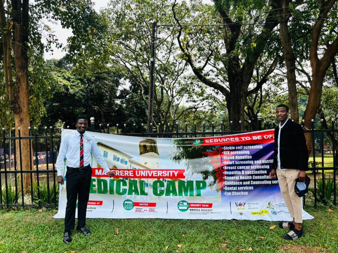 The 91st Guild Minister of Health, Hon. Bbosa Sharif (L) poses by the event banner in the Freedom Square. The 91st Guild Ministry of Health Annual Makerere Guild Medical Camp, 3rd and 4th October 2025, Freedom Square, Makerere University, Kampala Uganda, East Africa.
