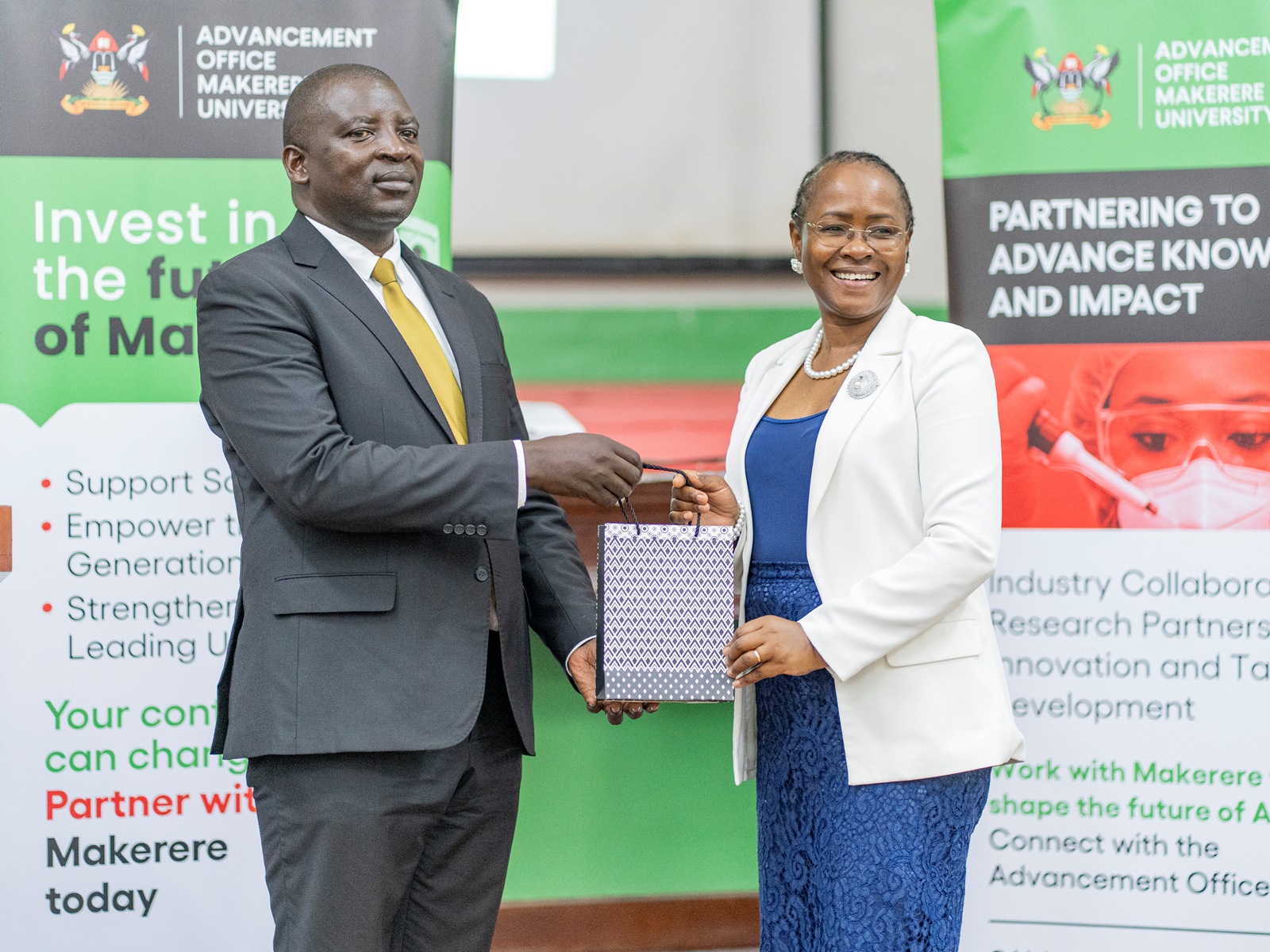 Hon. Eng. Cuthbert Abigaba (Left) receives Makerere Souvenirs from Prof. Sarah Ssali (Right). East African Universities Debate Championships 2026 (EAUDC ZAABU) Closing Ceremony, 31st July 2026, Main Hall, Makerere University, Kampala Uganda.