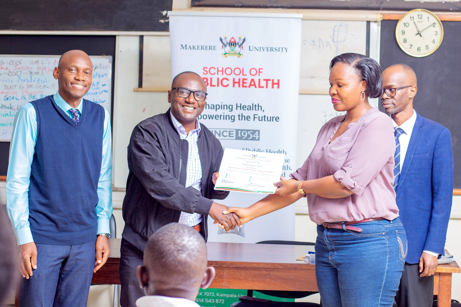 DJC's Dr. Ivan Lukanda presents a certificate to Kabasinguzi Grace. Makerere University School of Public Health (MakSPH) and Department of Journalism and Communication (DJC), College of Humanities and Social Sciences (CHUSS) graduation of 33 professionals from the second cohort of the Certificate in Health Communication and Community Engagement, 31st July 2026, Mulago Hospital Complex, Kampala Uganda, East Africa.