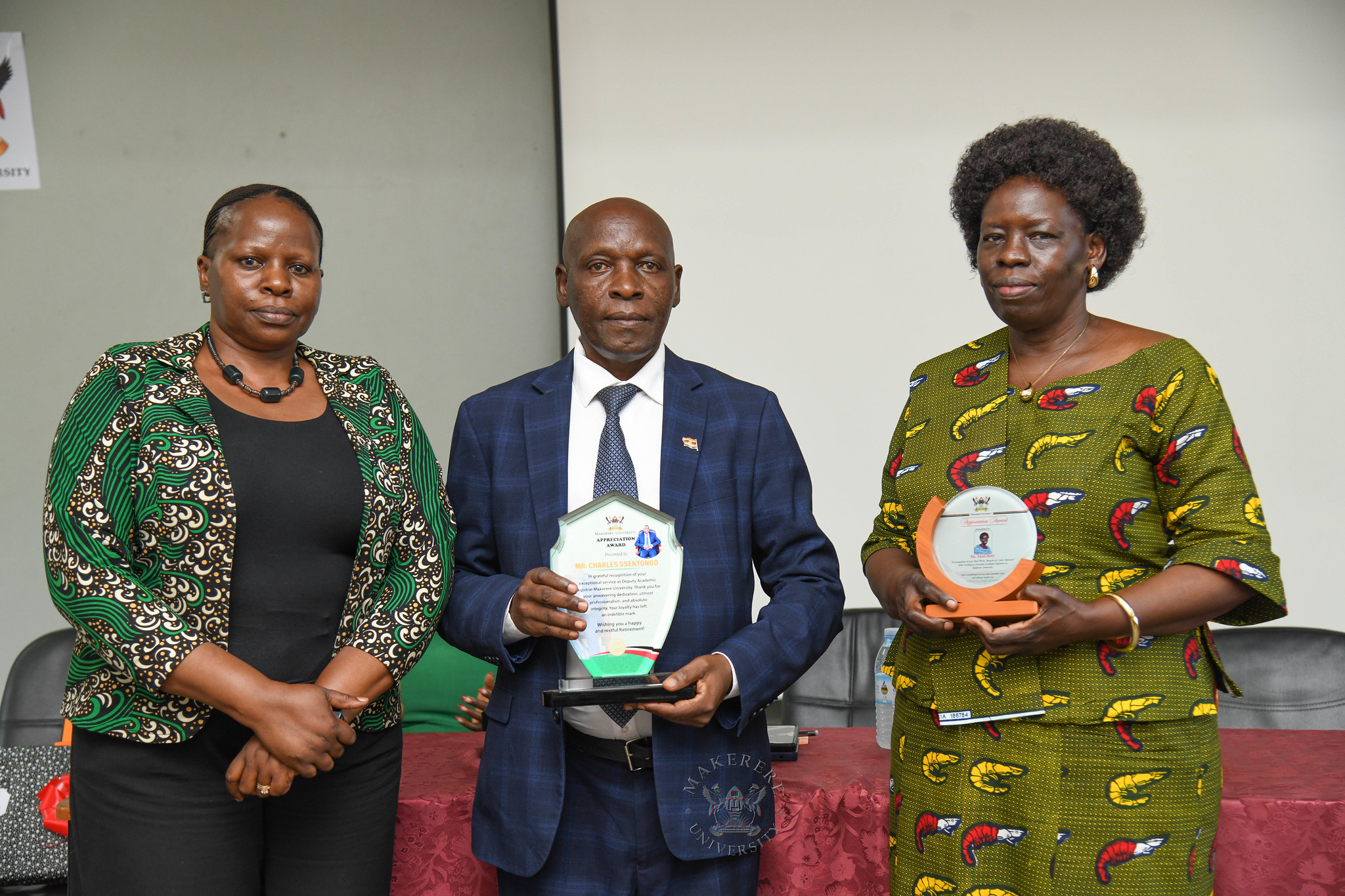 Ms. Prossie Nakayiki (L) poses with Mr. Ssentongo (C) and Ms. Akoli (R) shortly after presenting them with their plaques. Farewell Luncheon held by Department of Academic Registrar in honour of Mr. Charles Ssentongo, Deputy Academic Registrar – Undergraduate Admissions and Records and Ms. Betty Akoli, Assistant Academic Registrar presided over by Ag. Academic Registrar Ms. Prossie Nakayiki, 18th September 2026, Senate Conference Hal, Level 4, Senate Building, Makerere University, Kampala Uganda, East Africa.