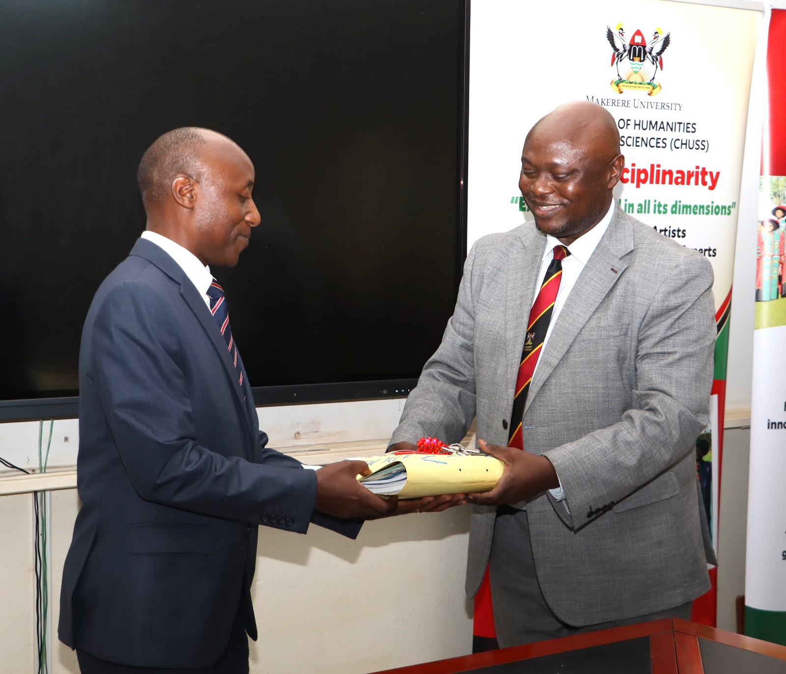 Incoming Deputy Principal CHUSS, Prof. Eddy Joshua Walakira (L) receives one of the Office files from outgoing counterpart Assoc. Prof. Eric Awich Ochen at the handover ceremony on 14th September 2026. Official Handover of Office of Deputy Principal, College of Humanities and Social Sciences (CHUSS), from Associate Prof. Eric Awich Ochen to Prof. Eddy Joshua Walakira, 14th September 2026, CHUSS Smart Room, Makerere University, Kampala Uganda, East Africa.