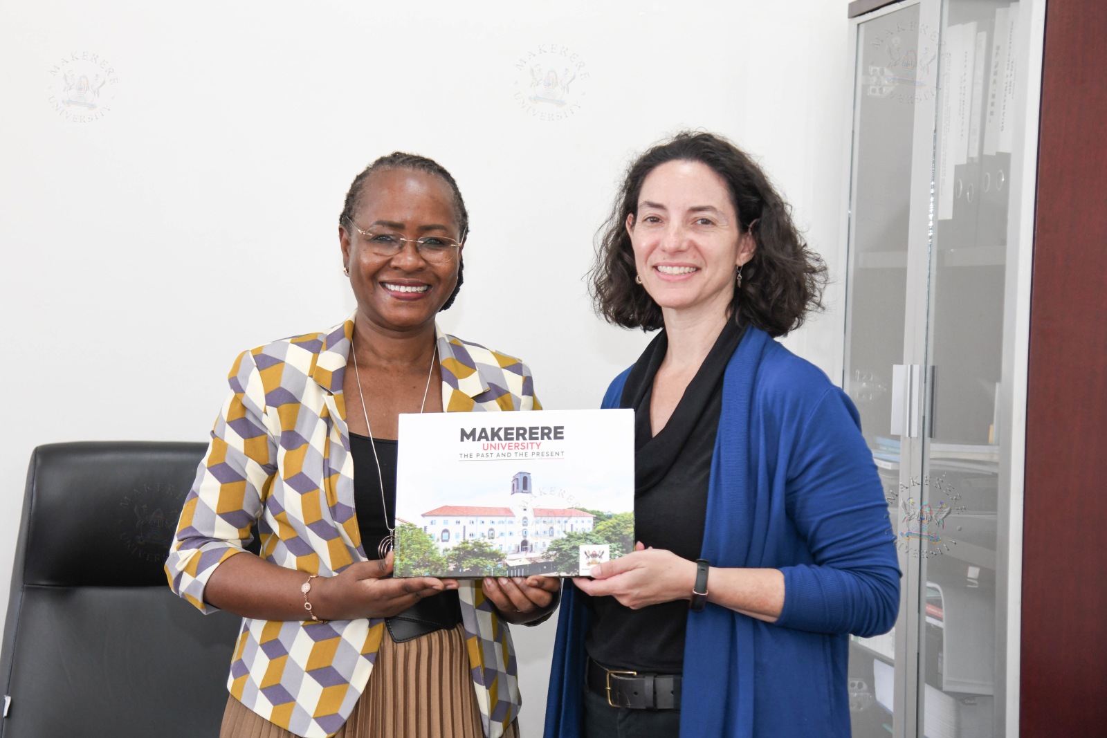 Prof. Sarah Ssali (L) presents the Makerere@100 Coffee Table book to Dr. Tracy Rabin (R). Courtesy call on Prof. Sarah Ssali, the Deputy Vice Chancellor in charge of Academic Affairs (DVCAA) by co-directors Dr. Tracy Rabin from Yale and Prof. Harriet Mayanja-Kizza from Makerere as the Makerere University–Yale University (MUYU) partnership celebrates two decades of collaboration in health education, clinical care, and applied research, 27th August 2026, Main Building, Makerere University, Kampala Uganda, East Africa.