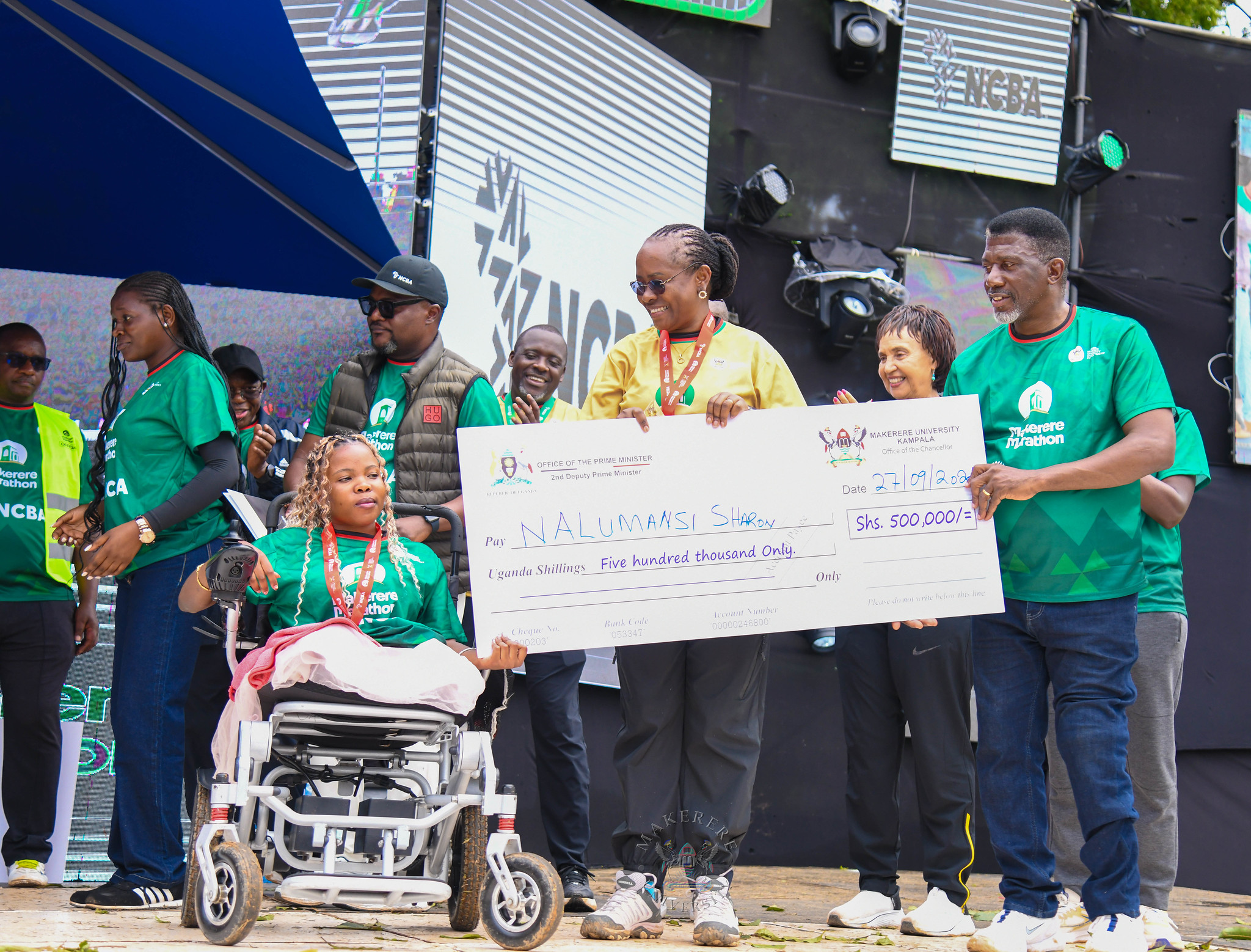 Ms. Nalumansi Sharon, winner of the 3km Wheelchair Race receives her dummy cheque from the DVCAA-Prof. Sarah Ssali (C) and Lord Mayor of Kampala City, HW Eng. Ronald Balimwezo (R). 6th Edition of the Makerere Marathon with Chief Runner as the Speaker of Parliament Rt. Hon. Jacob Marksons Oboth, 27th September 2026, Makerere University, Kampala Uganda, East Africa.