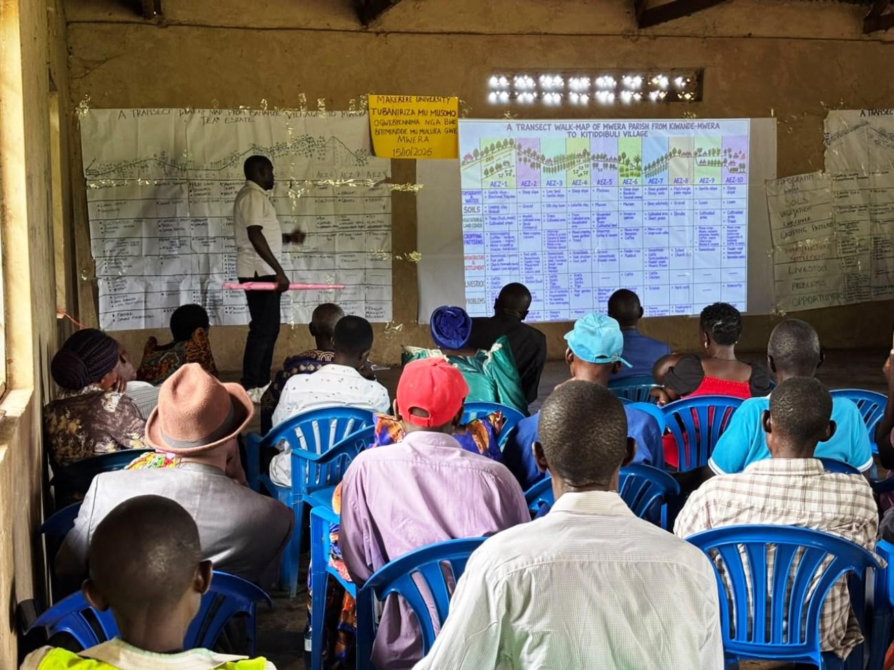 The community meeting underway at Mwera community hall with PhD student Ibrahim Mayanja explaining the Agri-ecological zones along the routes.PhD in Agricultural and Rural Innovation XIII, Department of Extension and Innovation Studies, College of Agricultural and Environmental Sciences (CAES), Makerere University Field Course, 4th-16th Oct 2026, Mwera Parish, Mityana District, Uganda, East Africa.